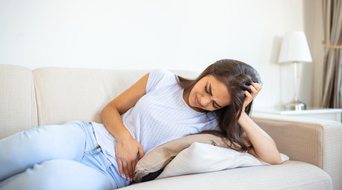 Mulher com dor abdominal deitada no sofá, ilustrando os sintomas da doença de Crohn que podem ser aliviados com cannabis